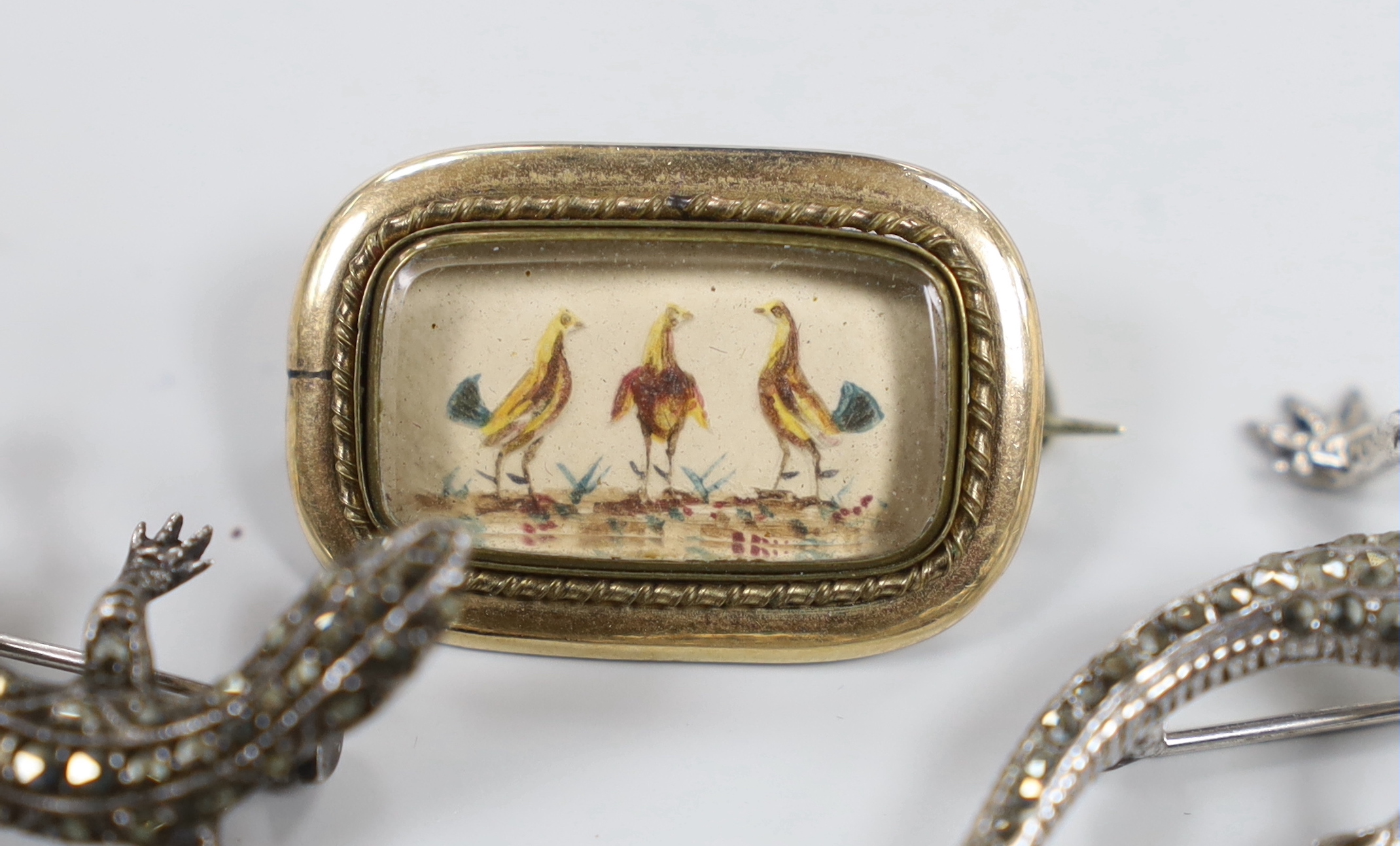 A 1920's French white metal and paste set etched glass brooch, 53mm, two marcasite lizard brooches and a Victorian yellow metal mounted brooch, decorated with three cockerel.